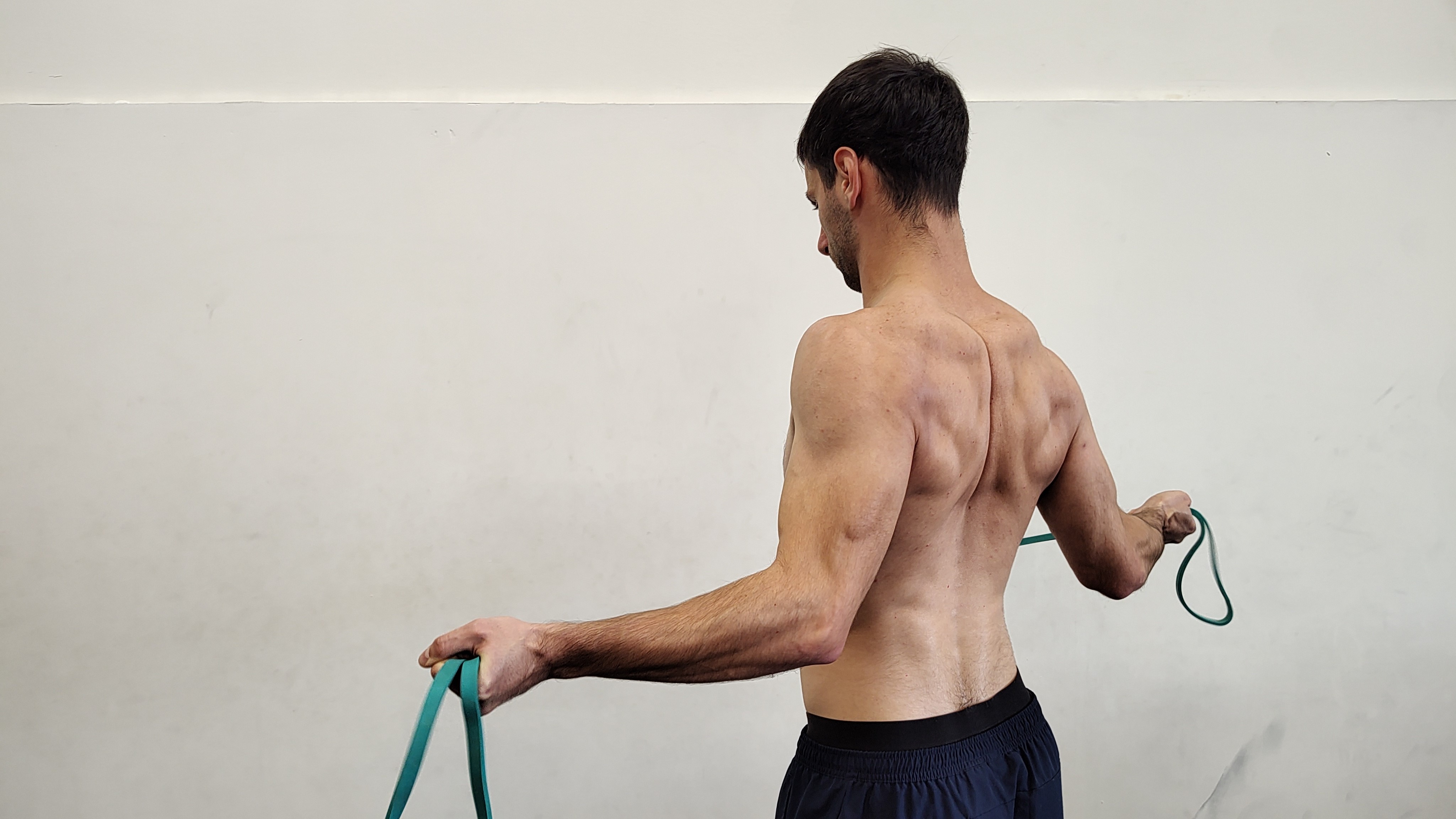 Muž v tělocvičně cvičí s expanderem lopatkové svaly.